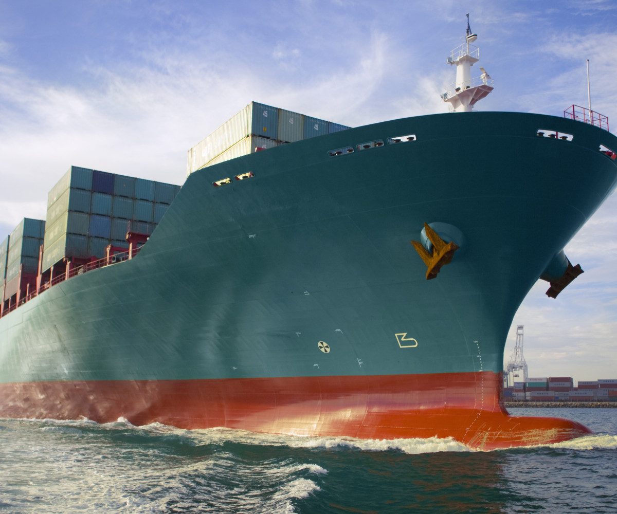 Bow view of loaded cargo ship sailing out of port.